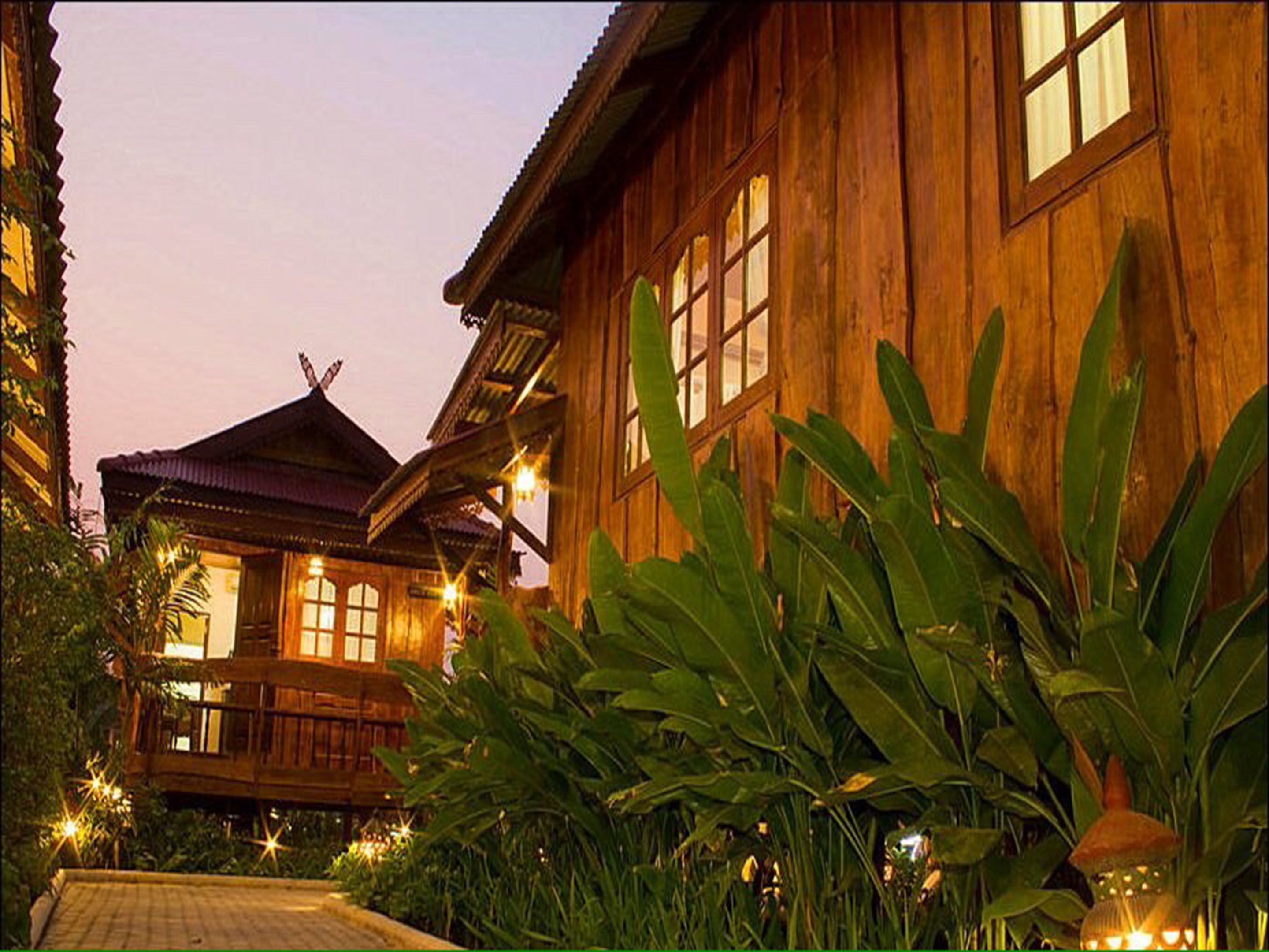 A wooden building with large windows and a balcony, surrounded by lush greenery.