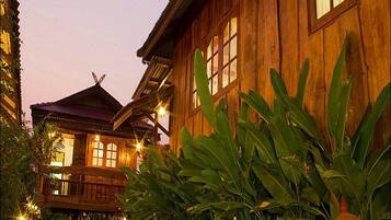 A wooden building with large windows and a balcony, surrounded by lush greenery.
