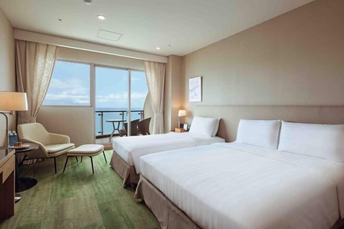 Habitación de hotel con dos camas, un escritorio, una silla, una mesita y vistas al cielo.