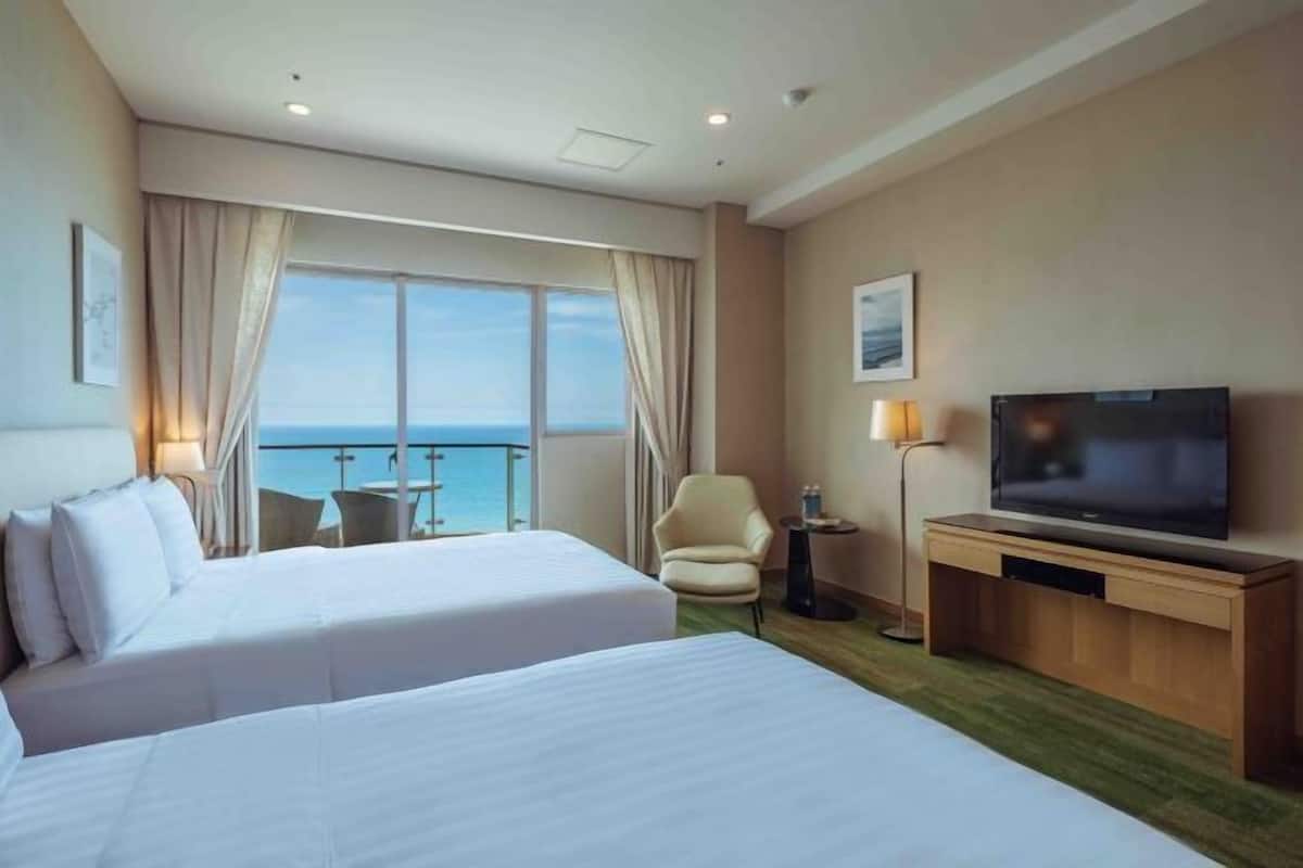 Habitación de hotel con dos camas, televisión, una silla y vista al mar.