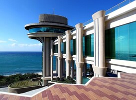 Un edificio moderno con una torre circular, ventanas amplias y vista al océano.