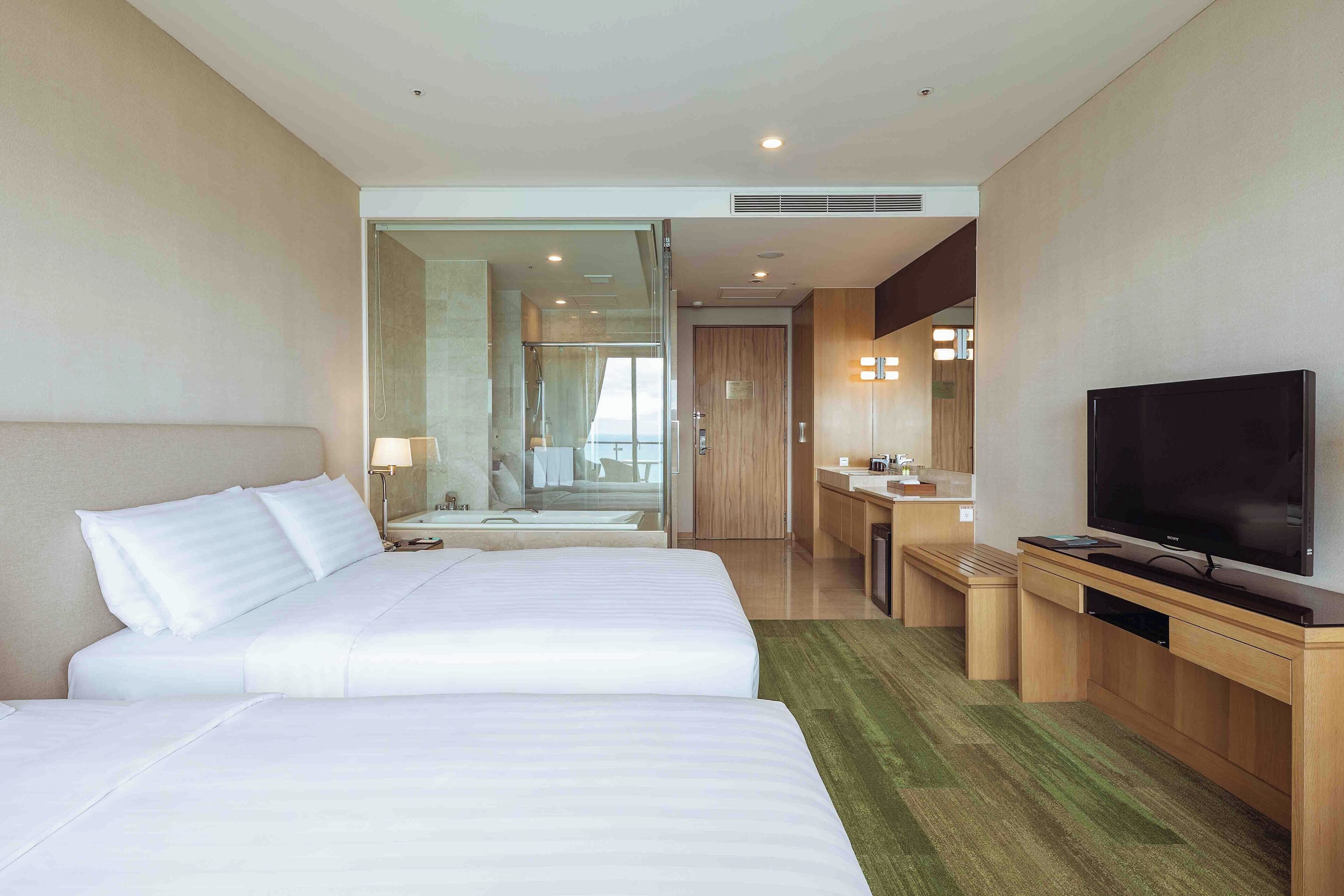 Une chambre d’hôtel avec deux lits, une télévision, un bureau et une salle de bain visible à travers une porte en verre.