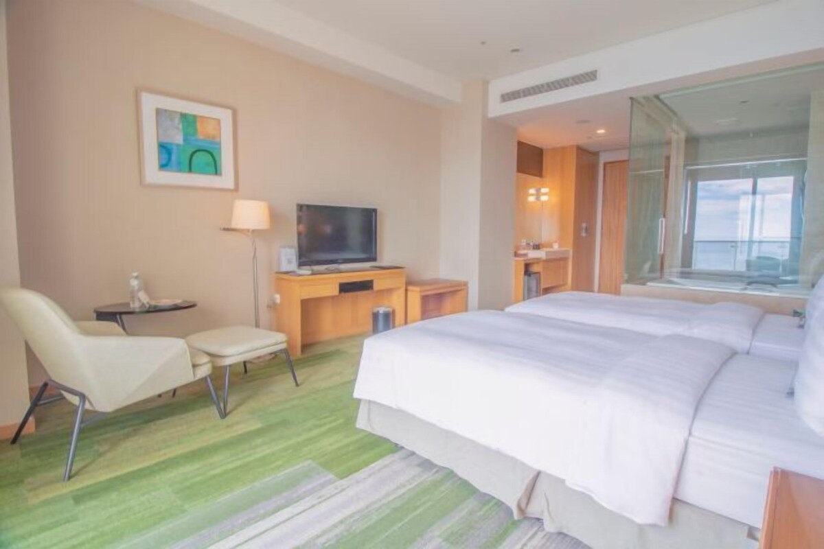 Une chambre d’hôtel avec un lit, un bureau avec une télévision, une chaise, une petite table et une fenêtre.