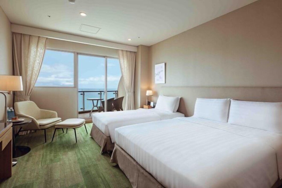 Une chambre d’hôtel avec deux lits, un bureau, une chaise, une petite table et une vue sur le ciel.