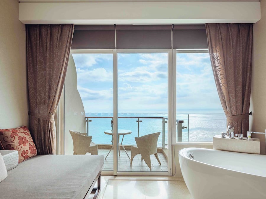 Een hotelkamer met balkon, bed, badkamer en uitzicht op zee.