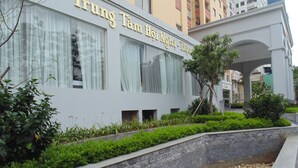A modern building with a sign reading "Trung Tam Hoi Nhat Nhat." It features large windows, a landscaped garden with shrubs and a small water feature, and is surrounded by other buildings. - Sport Hotel (Hanoi)