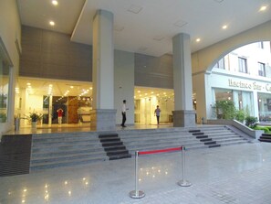 L’entrée d’un hôtel au design moderne, caractérisée par une façade en verre, un escalier menant à l’entrée et une barrière en corde rouge.