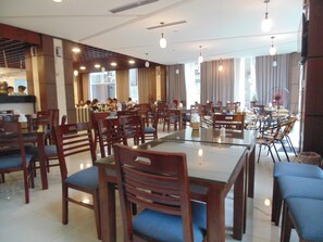 Un vaste espace dédié à la salle à manger, avec de nombreuses tables et chaises, de grandes fenêtres agrémentées de rideaux et un design de plafond moderne.