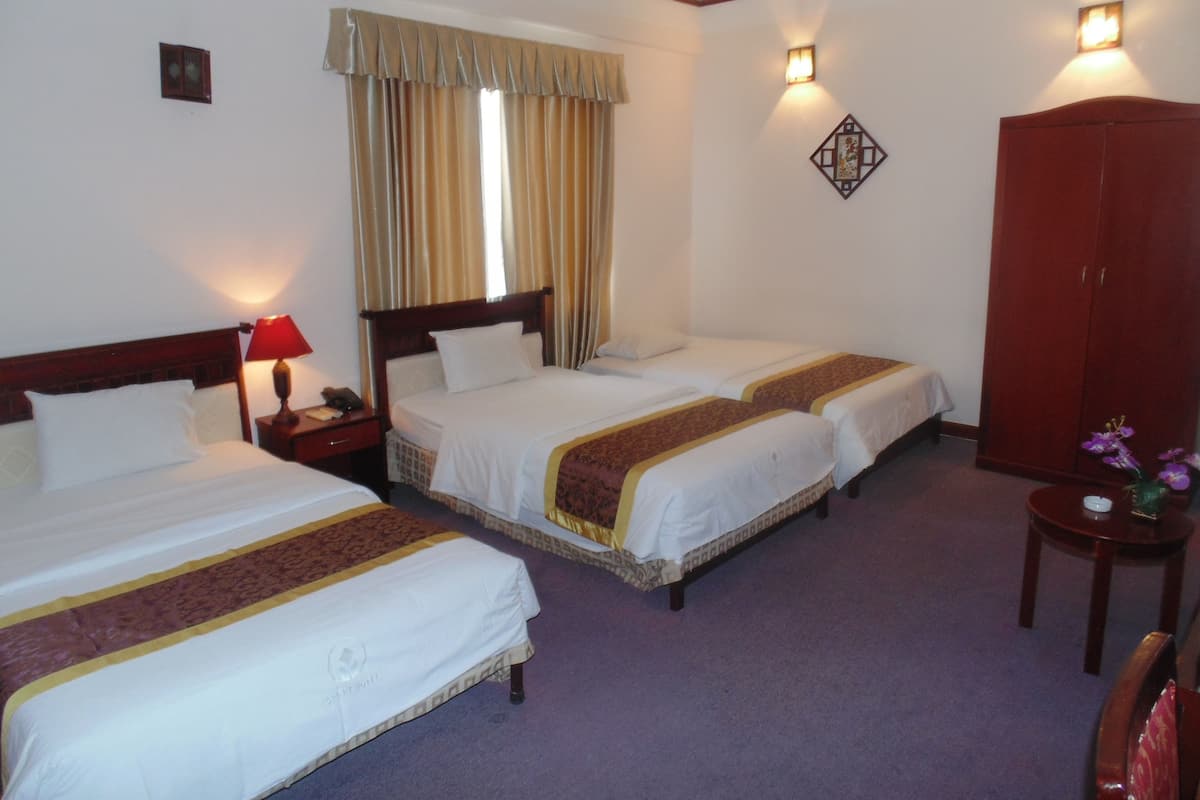 A hotel room with two single beds, a wooden wardrobe, a small table with a vase, and a wall-mounted light fixture.