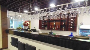 A bar area with a long counter, multiple bar stools, and a variety of glassware and bottles on shelves. - Sport Hotel (Hanoi)