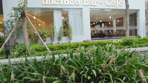 A cafe named 'Hacimco Bar Cafe' with a modern facade, large windows, and a well-maintained outdoor garden area. - Sport Hotel (Hanoi)