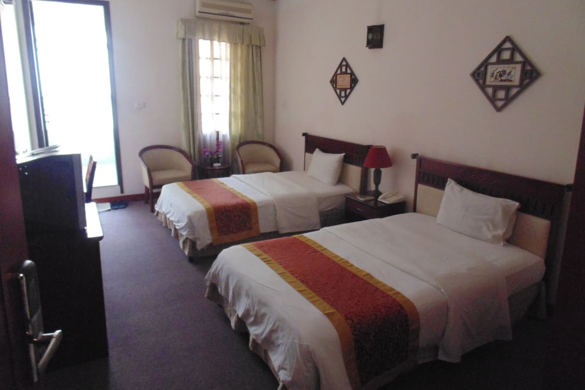A hotel room with two single beds, a desk, a chair, an air conditioning unit, and a window with curtains.