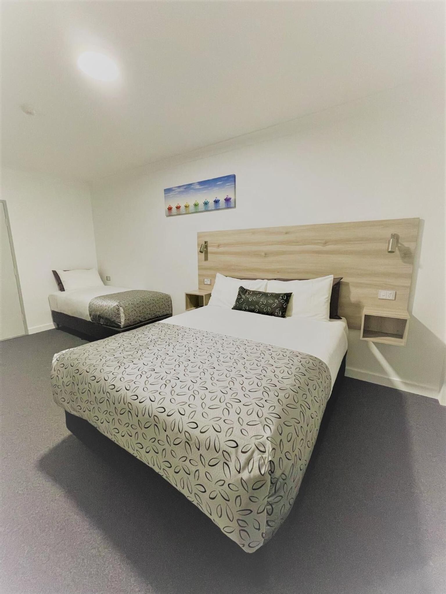 Une chambre d’hôtel avec un grand lit, une table de chevet, une commode et une lampe fixée au mur.
