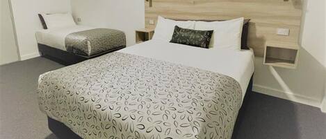 Une chambre d’hôtel avec un grand lit, une table de chevet, une commode et une lampe fixée au mur.