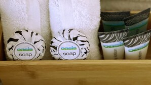 Un estante de madera con varios artículos de aseo, incluyendo toallas blancas, una toalla mullida blanca y jabones de barra con diseños variados.