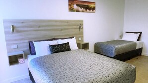 Habitación de hotel con dos camas, cabecera de madera, mesita de noche pequeña y un cuadro colgado en la pared.