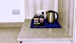 Un coin cuisine comprenant un plan de travail, une machine à café, une boîte de biscuits et une étagère avec de la verrerie.
