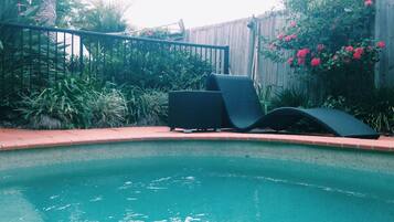 A swimming pool with two lounge chairs and a wooden fence in the background.
