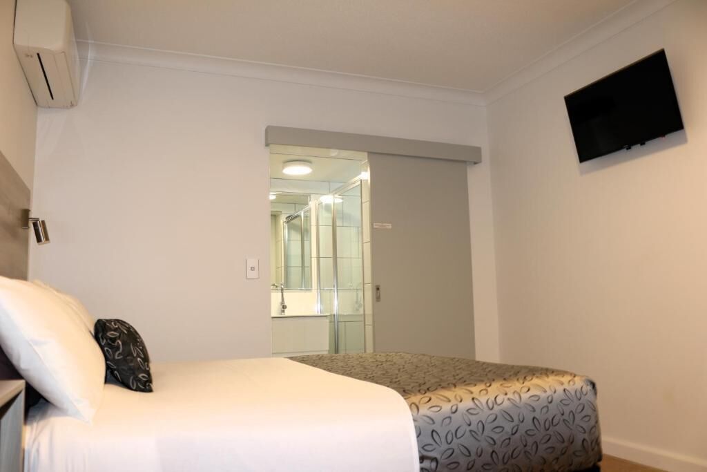 A bedroom with a bed, a television mounted on the wall, and a bathroom visible through an open door.