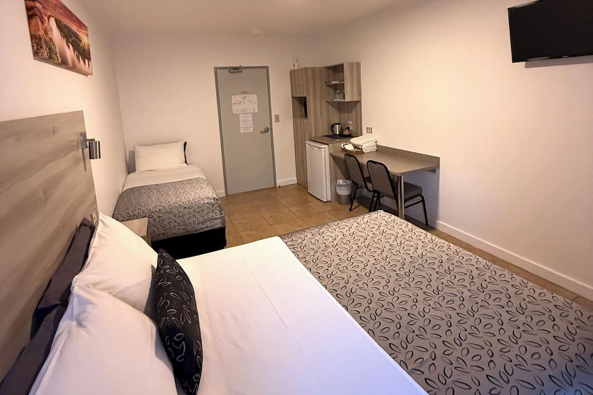 Habitación de hotel con dos camas, un escritorio, una silla, una kitchenette pequeña y una puerta.
