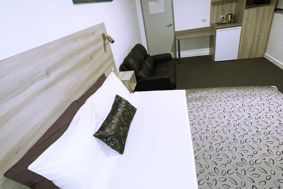 Habitación de hotel con cama, escritorio, silla y una pequeña kitchenette.