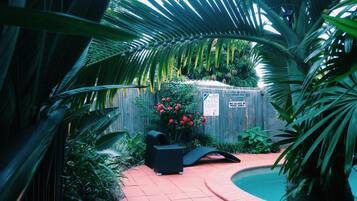 Uma área de piscina com cerca de madeira, uma cadeira de sol preta e flores vermelhas.