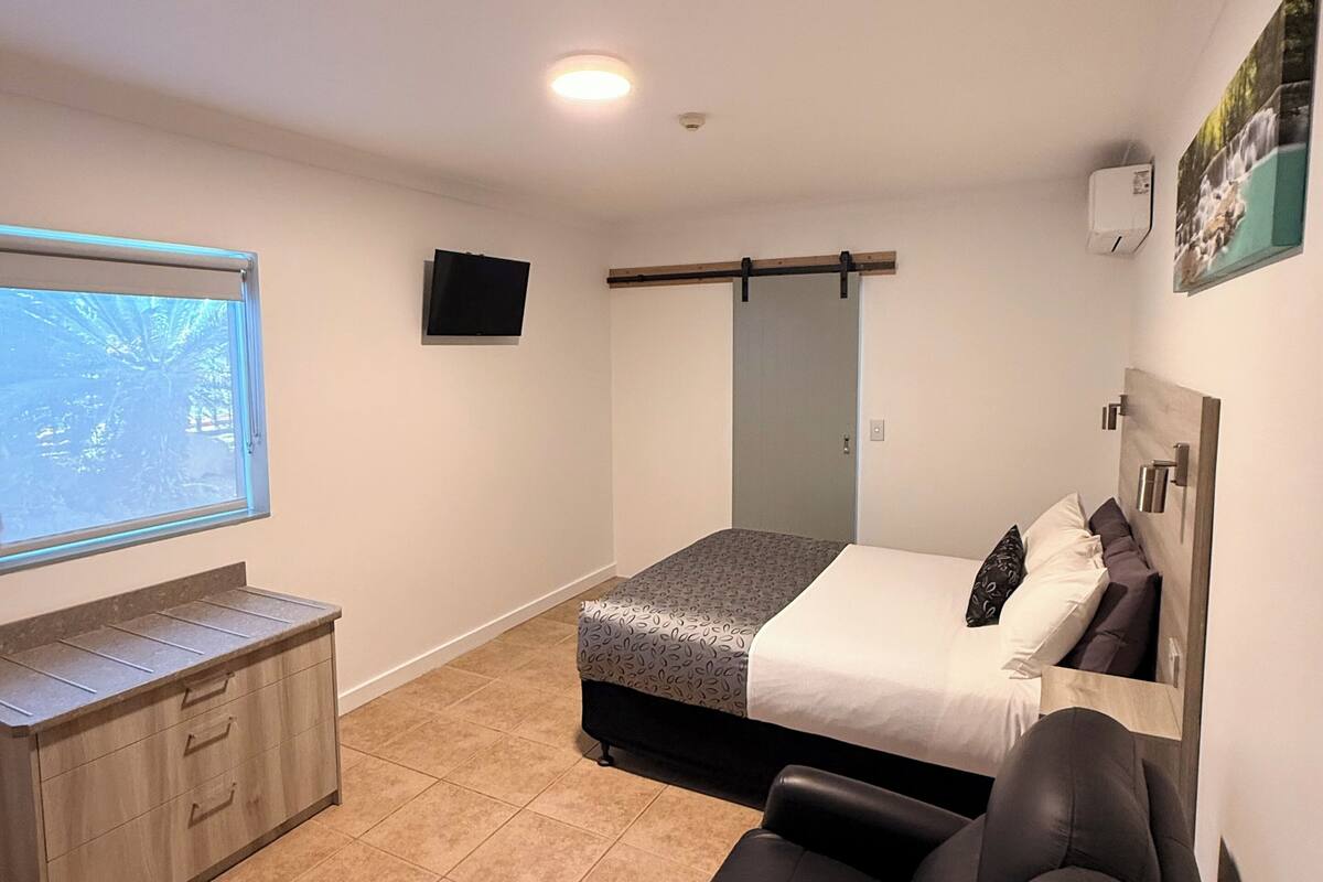 Un dormitorio moderno con cama, televisión, sofá y ventana con vistas.