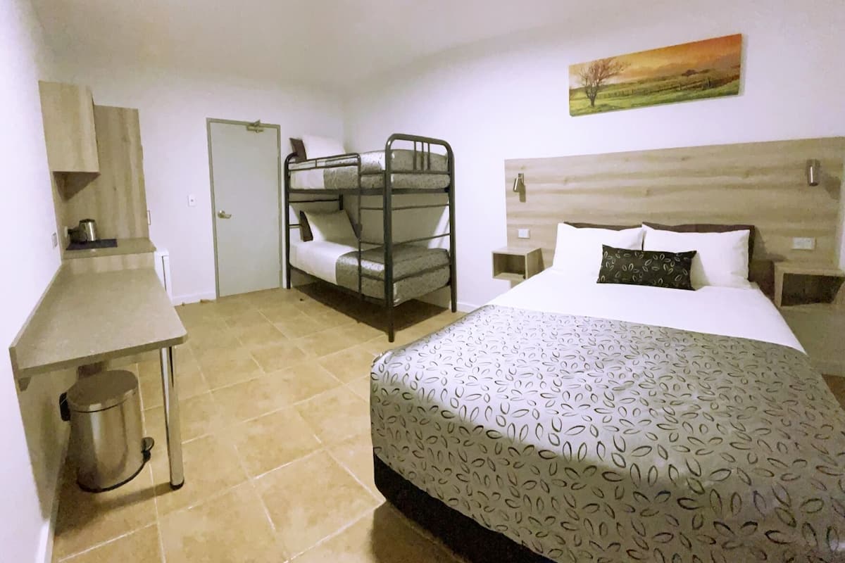Una habitación con una cama individual, una litera, una pequeña kitchenette y un cuadro en la pared.