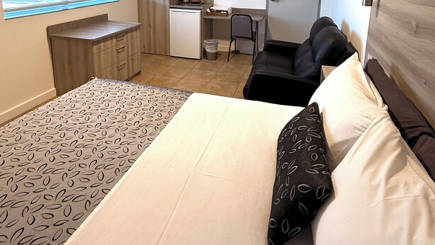 Una habitación de hotel compacta con cama, escritorio, silla y kitchenette.