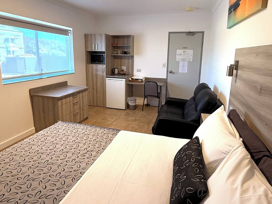A compact hotel room with a bed, a desk, a chair, and a kitchenette.