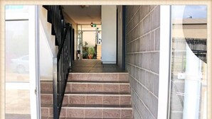 Un escalier menant à un espace intérieur doté d’un mur carrelé et d’une rambarde en métal.
