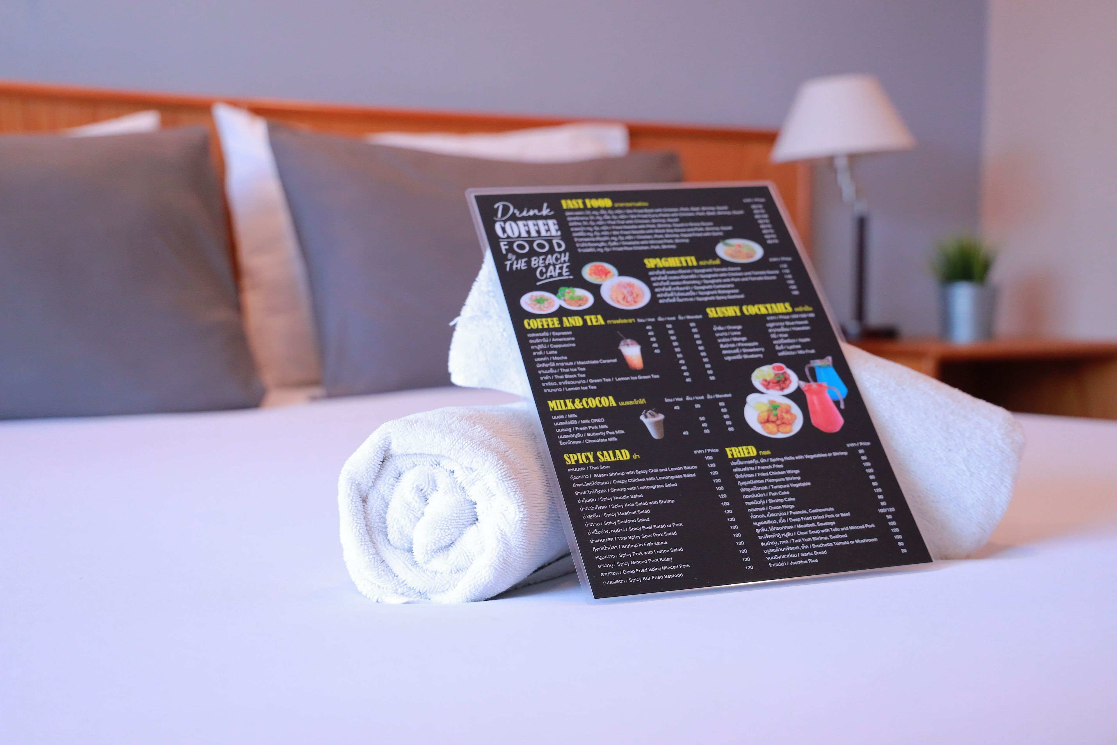 A menu on a bed with pillows, a lamp, and a plant in the background.
