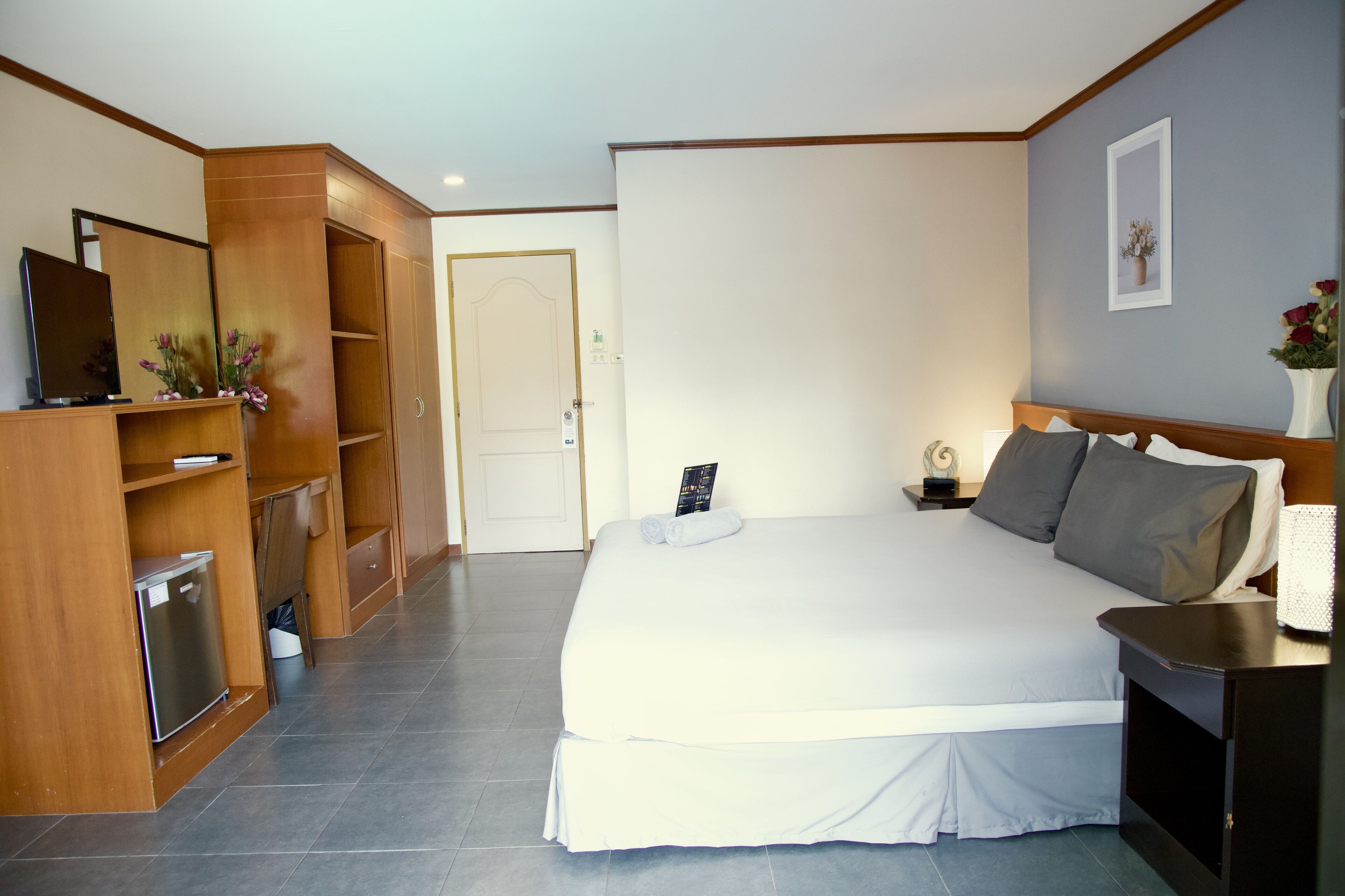 Quarto de hotel com cama, televisão, escrivaninha e guarda-roupa.