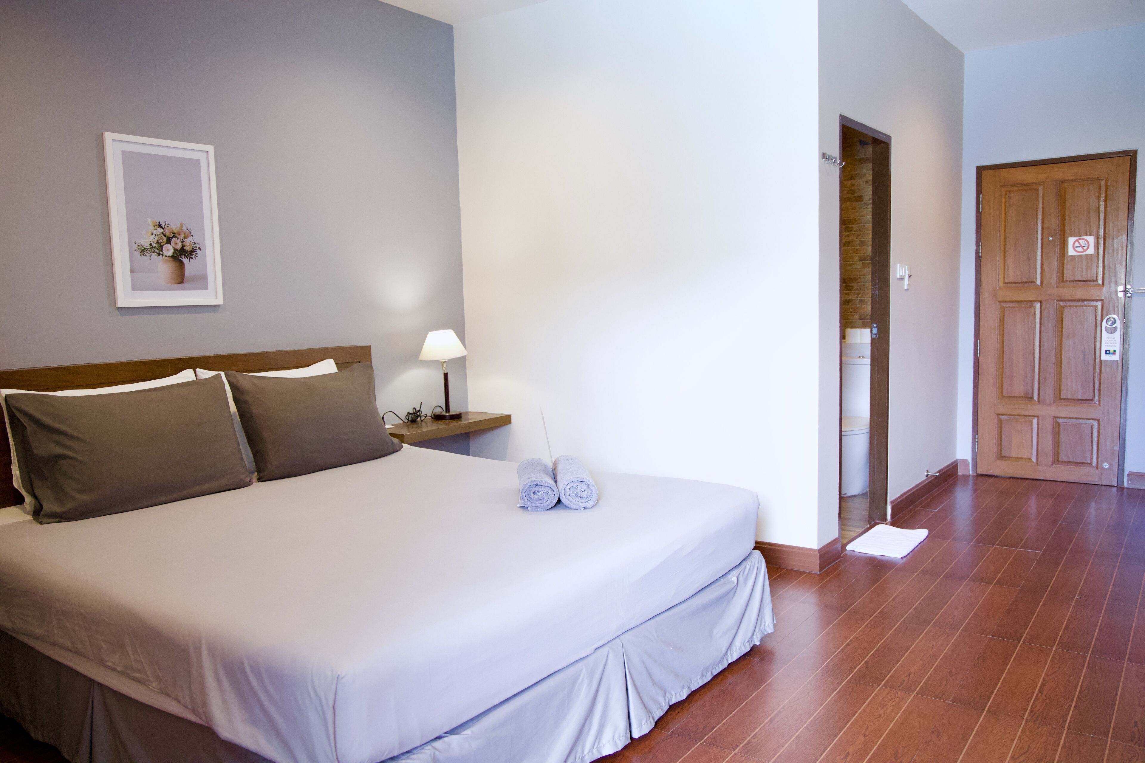 A hotel room with a bed, a nightstand with a lamp, a framed picture on the wall, and a wooden door.