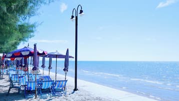 A beach with rows of striped beach chairs and umbrellas, a tall street lamp, and a clear view of the sea.