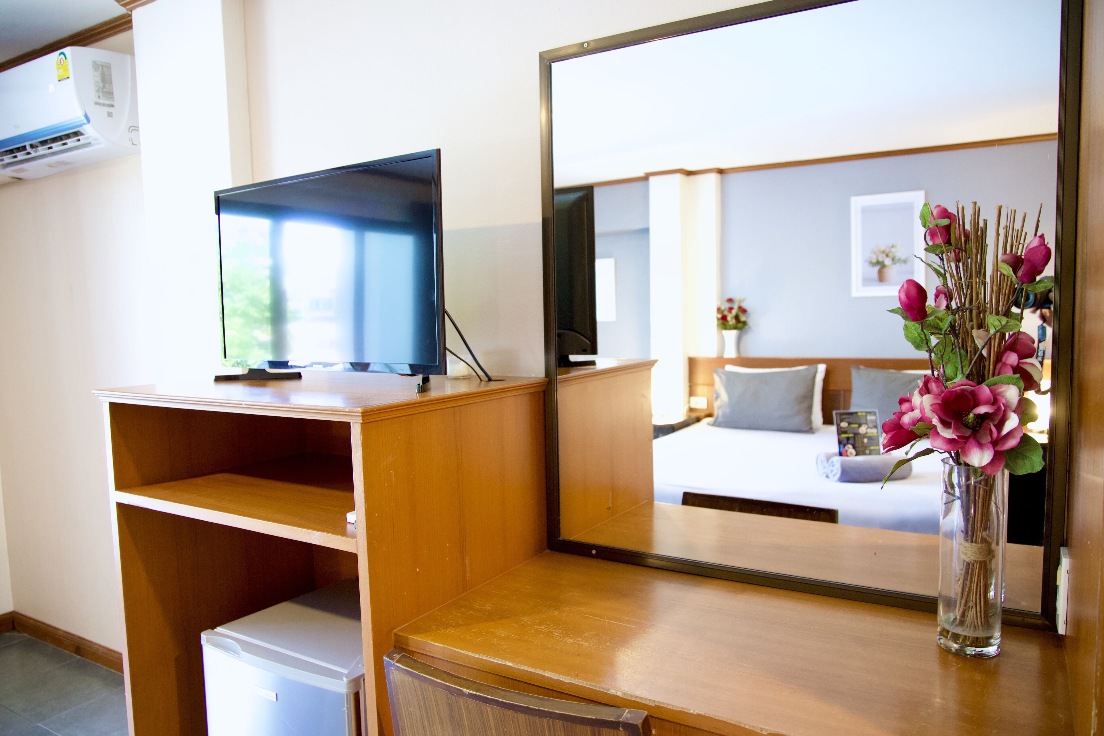 Une chambre d’hôtel avec un bureau en bois, une télévision, un miroir et un vase de fleurs.