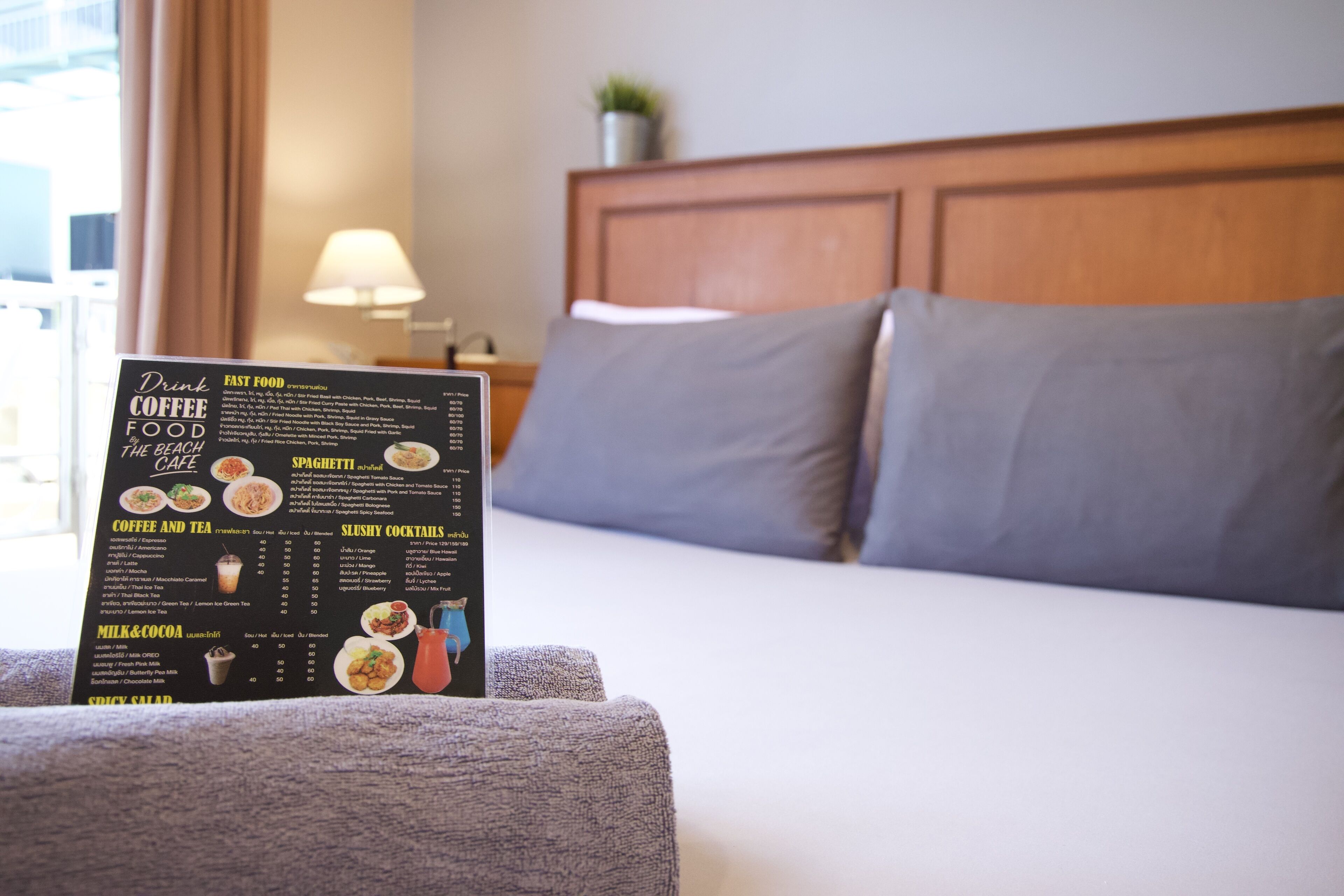 Ein Hotelzimmer mit Bett, Nachttisch, Lampe und einer Speisekarte auf dem Bett.