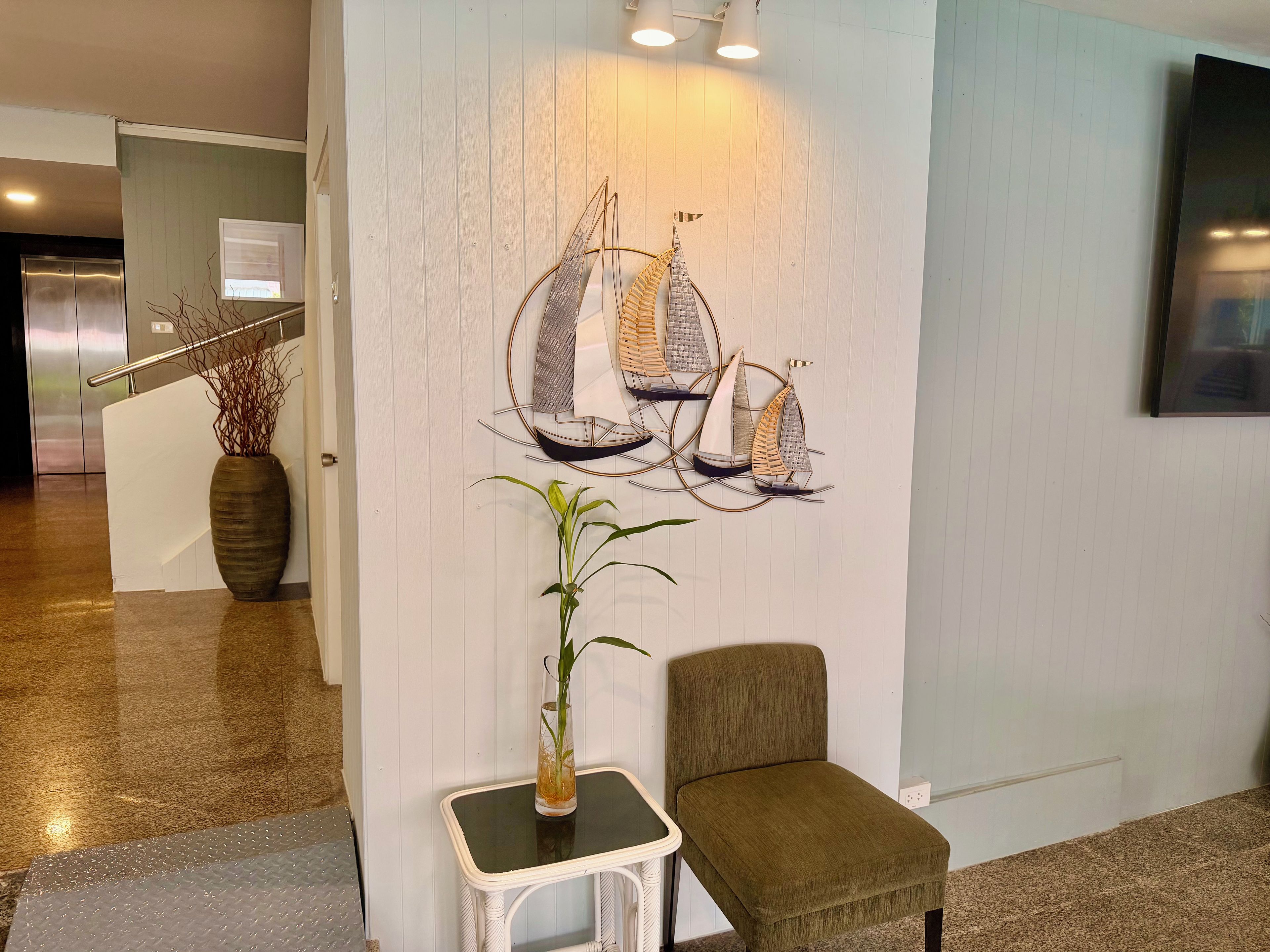 Un vestíbulo con una decoración de velero en la pared, una planta en maceta, una pequeña mesa y un sillón acolchado.