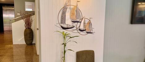 Un vestíbulo con una decoración de velero en la pared, una planta en maceta, una pequeña mesa y un sillón acolchado.
