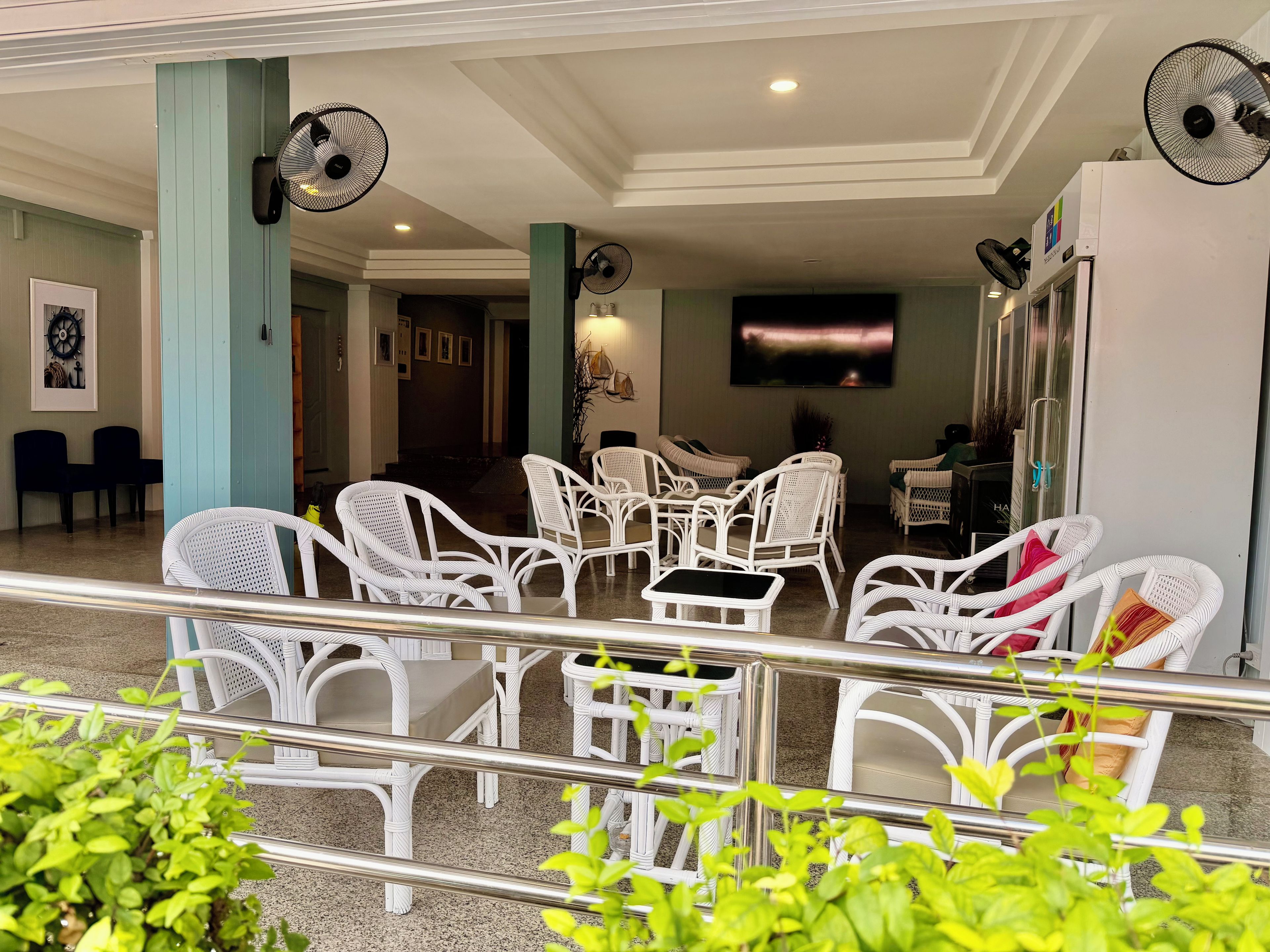 A hotel lobby with white wicker furniture, ceiling fans, a flat-screen TV, and a staircase leading to other areas.