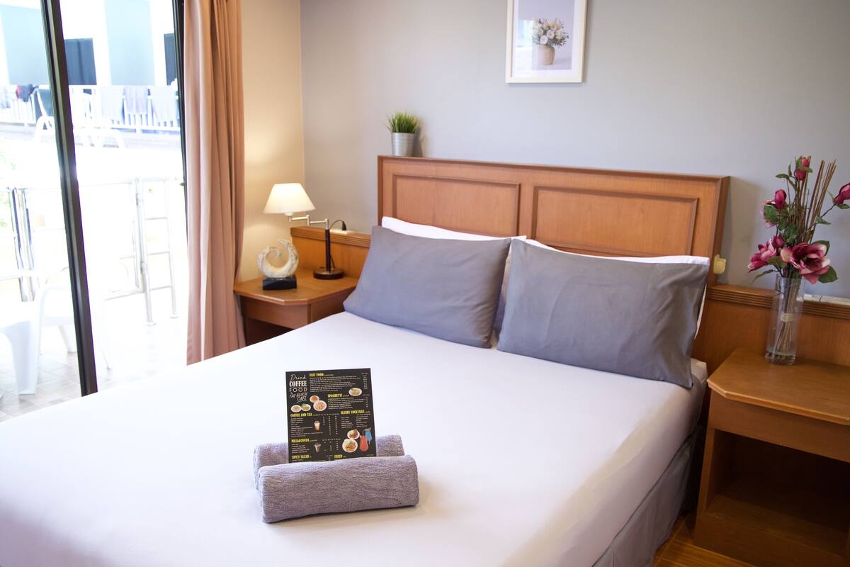A neatly made bed with a menu, a lamp, and a vase with flowers on the side table.