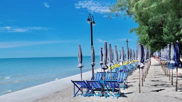 A beach with rows of blue lounge chairs and umbrellas, a clear sky, and the ocean in the background.