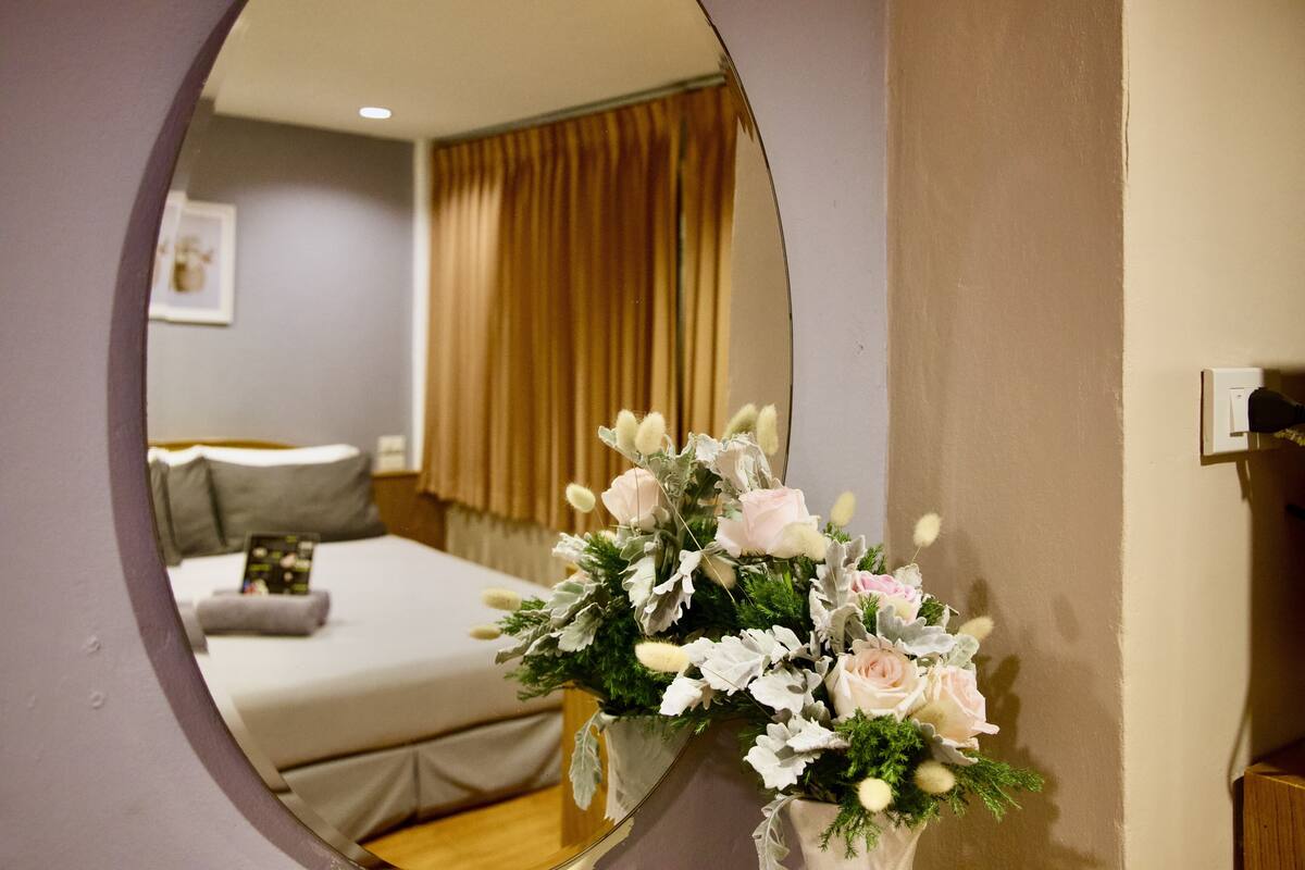 A bedroom with a bed, a mirror, and a floral arrangement.