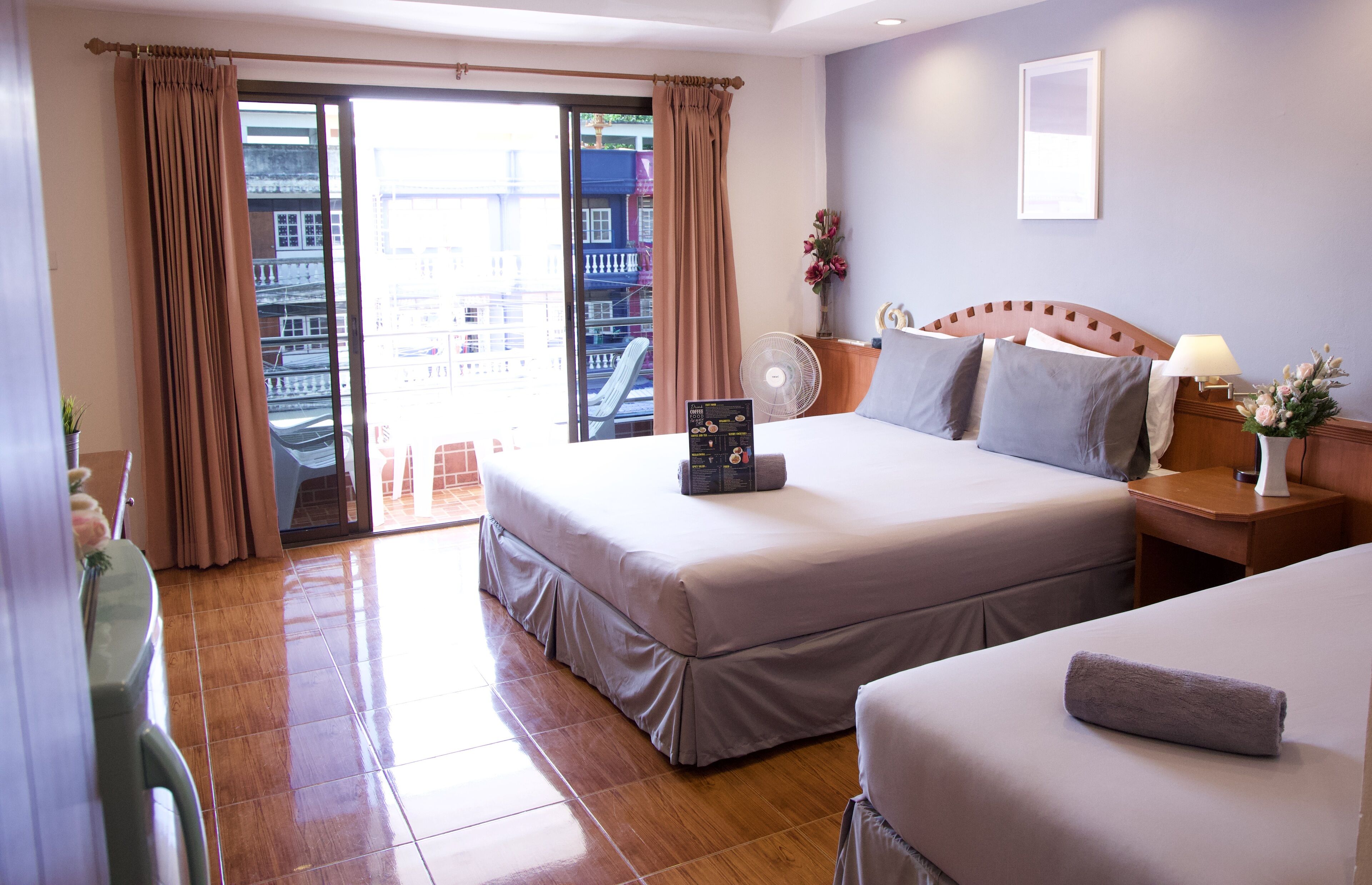 Una habitación de hotel con una cama grande, una cama más pequeña, un escritorio, una silla, un ventanal con cortinas y vistas a edificios.