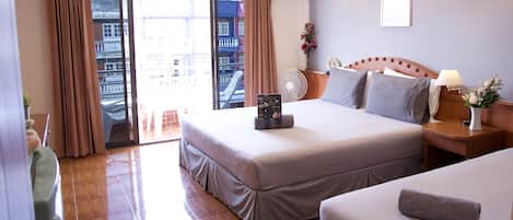 Una habitación de hotel con una cama grande, una cama más pequeña, un escritorio, una silla, un ventanal con cortinas y vistas a edificios.