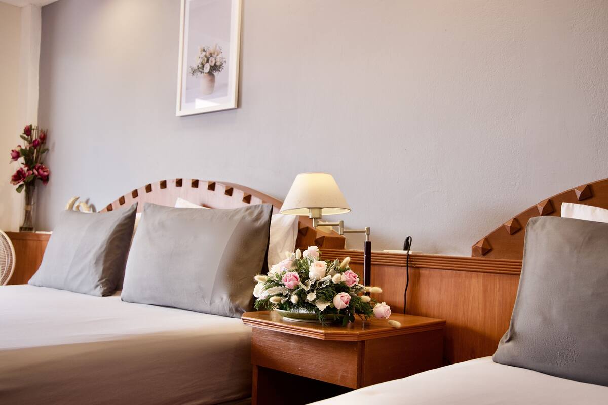 A hotel room with two beds, a nightstand with a lamp, and a framed picture on the wall.