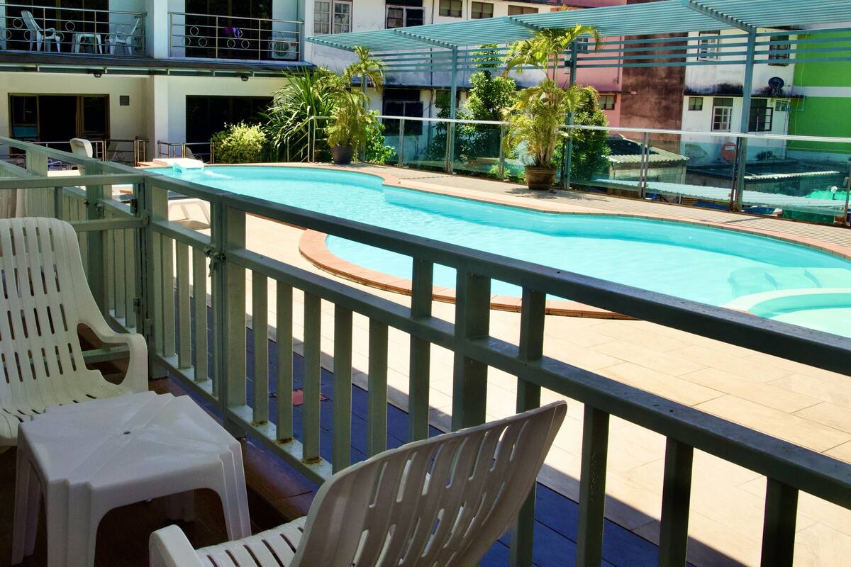 A pool area with a view of a building with multiple balconies and potted plants.