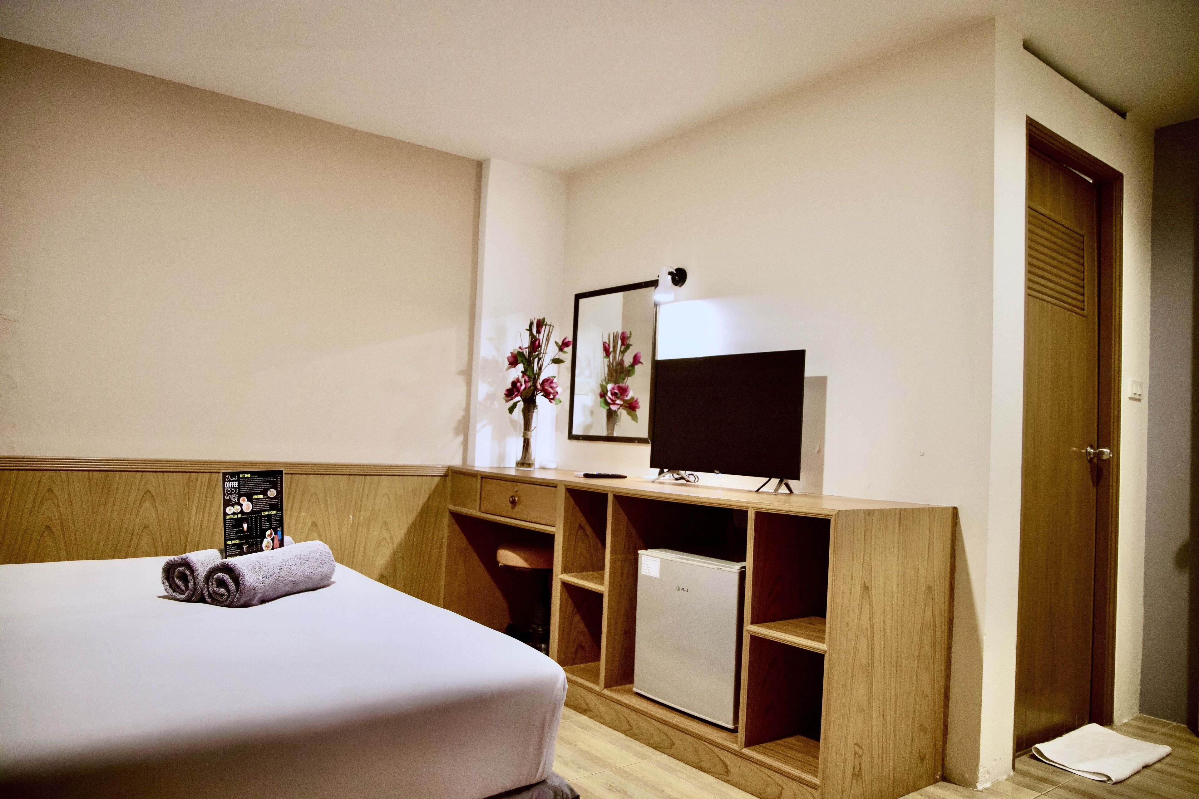 A hotel room with a bed, a desk, a mirror, a TV, and a wardrobe.