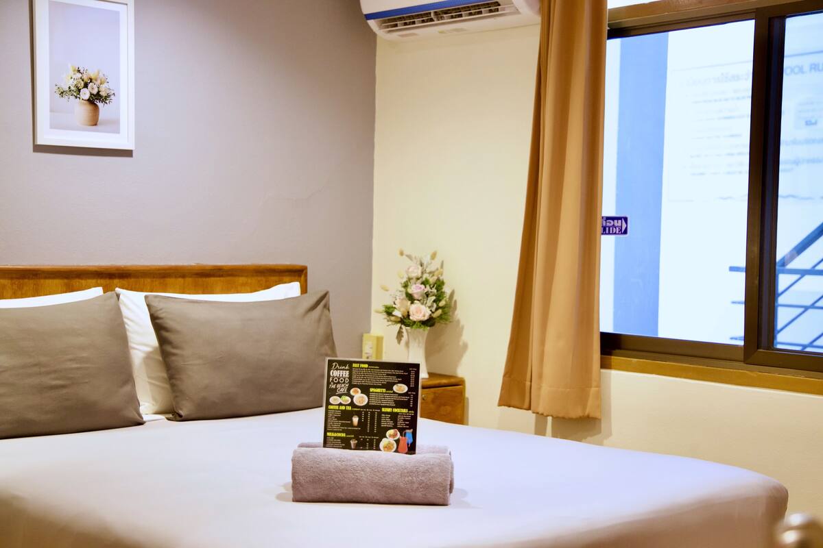 A neatly made bed with a menu on it, a vase of flowers, and a window with curtains.