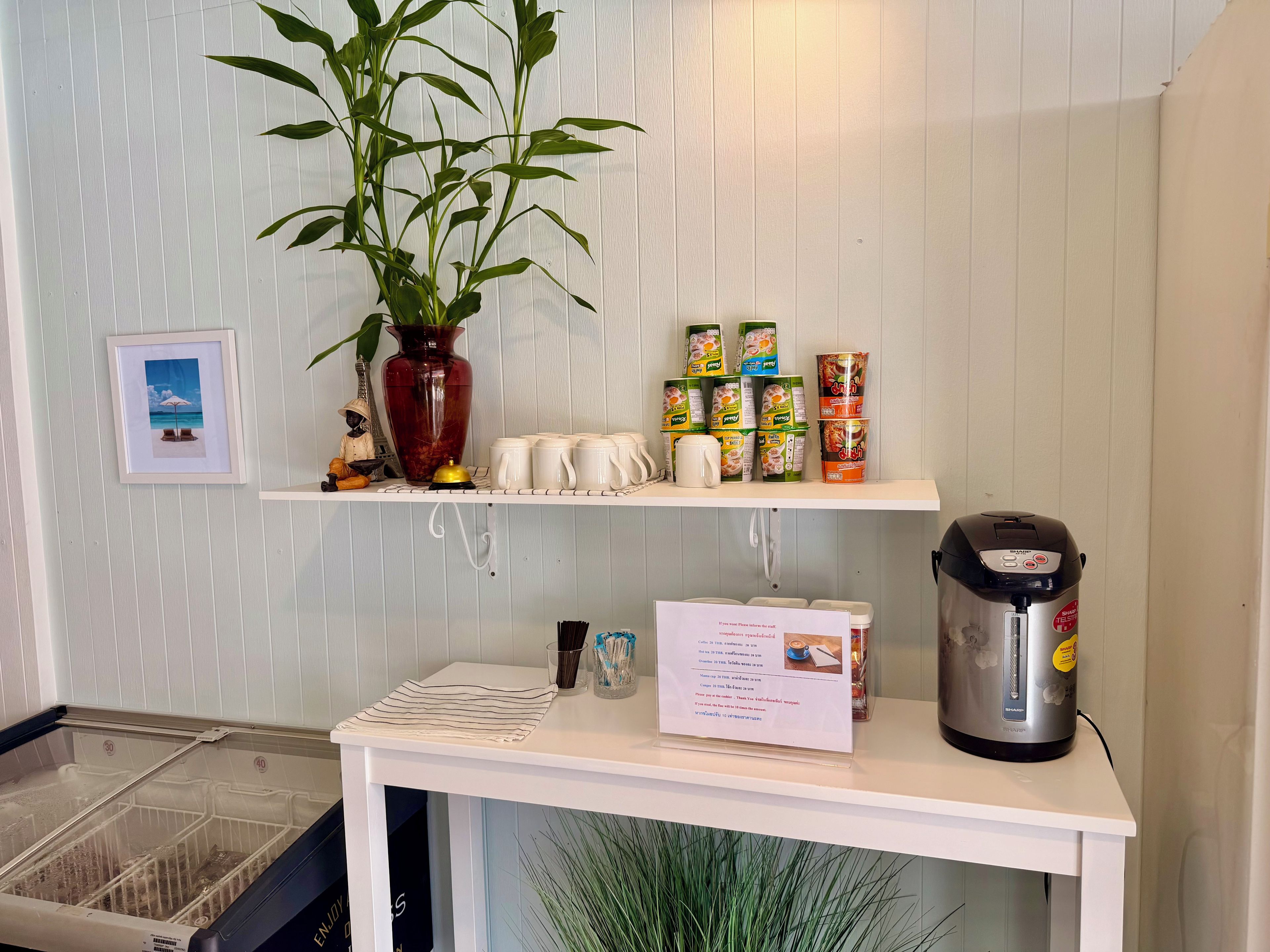 A kitchen area with a white countertop, a coffee maker, a vase with a plant, and various food containers.